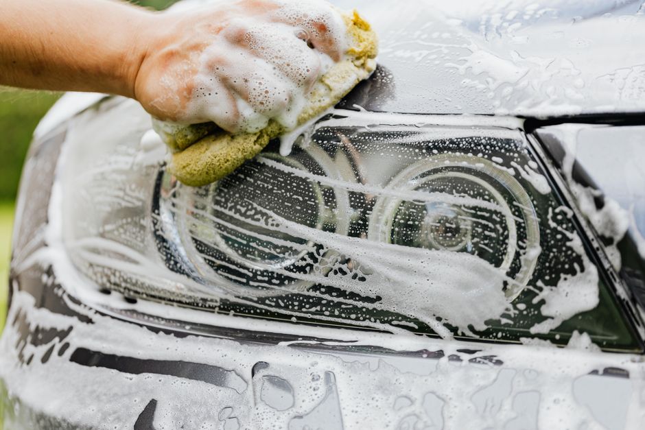 Detailer scrubbing a car headlight with a sponge and suds.