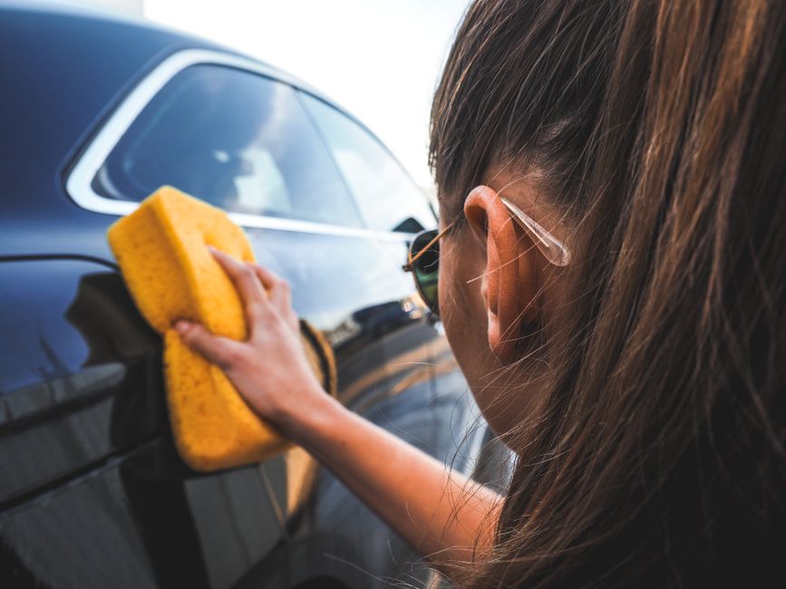 Detailer hand-washing a black car with a yellow sponge.